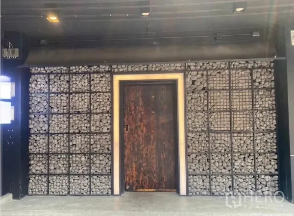 店屋 出租 - 店面外立面采用石笼墙与复古木门，配有暗色雨棚灯光。