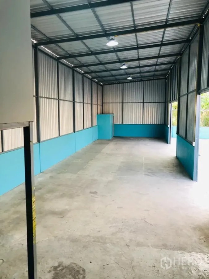Warehouse for rent in Saphan Sung, Bangkok - Long interior aisle of the warehouse showing overhead lights, turquoise lower walls and smooth concrete floor.