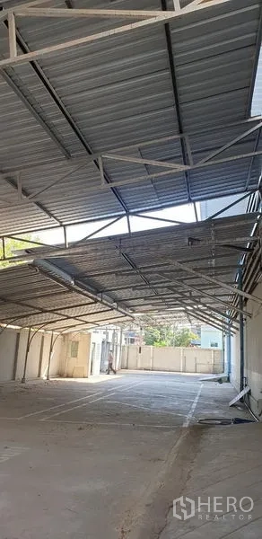 Warehouse for rent in Lam Luk Ka, Pathum Thani - Large covered parking and loading area with metal truss roof beside the warehouse.