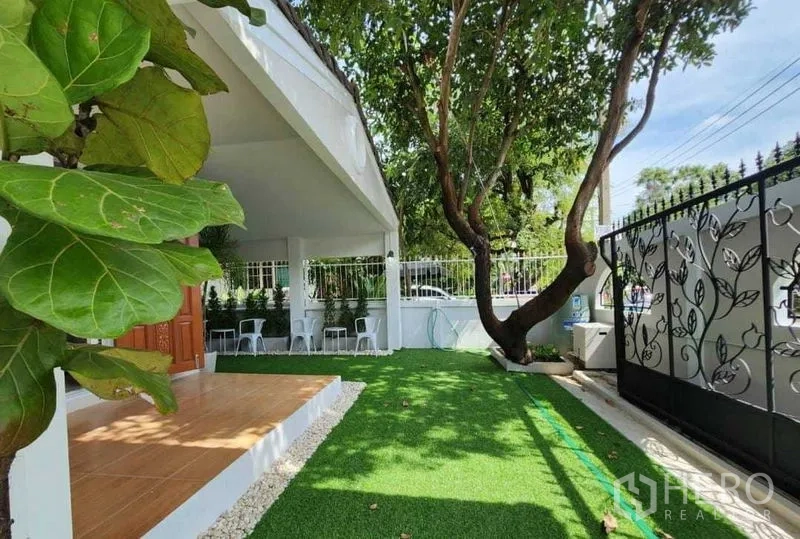 Detached House for rent in Lam Luk Ka, Pathum Thani - Front garden with big tree, artificial grass and wrought-iron gate.