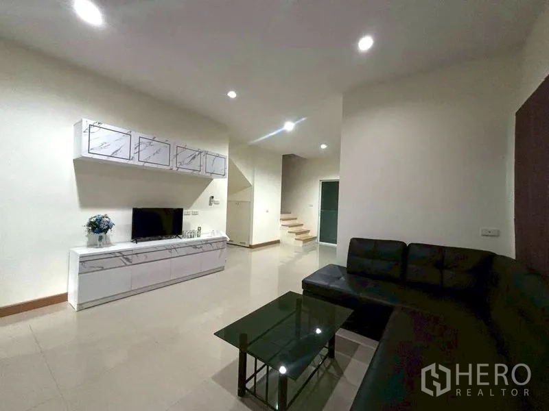 Townhouse for rent in Suan Luang, Bangkok - Bright living room with L-shaped sofa, TV console, and ceiling lights.
