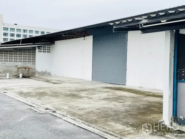 工厂 出租在Bang Pakong, Chachoengsao - 单个仓库开间，卷帘门与充足装卸空间，旁有矮砌块墙。