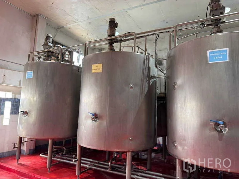 Factory for sale in Samut Prakan - Row of large stainless steel storage tanks with valves in a processing area.