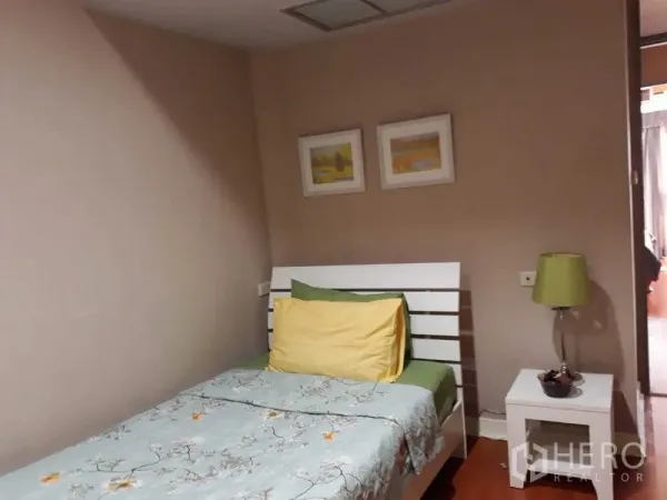 Condominium for rent or sale in Khlong Toei, Bangkok - Cozy single bedroom with white bed, bedside table and lamp, neutral walls and framed art in a Sukhumvit condo.