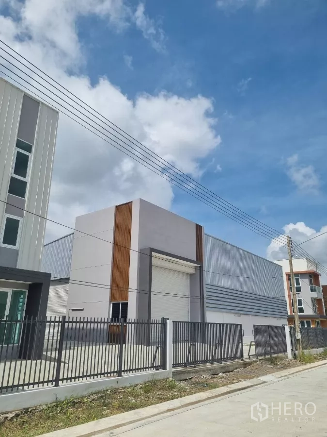 Warehouse for sale in Lam Luk Ka, Pathum Thani - Close street view of warehouse roller shutter bay and fence.