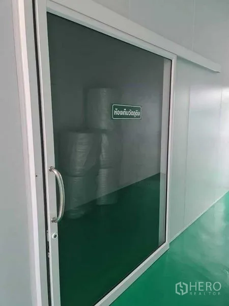 Factory for sale in Bang Pa-in, Phra Nakhon Si Ayutthaya - Sliding glass door to the raw-material storage room with stacked rolls inside.