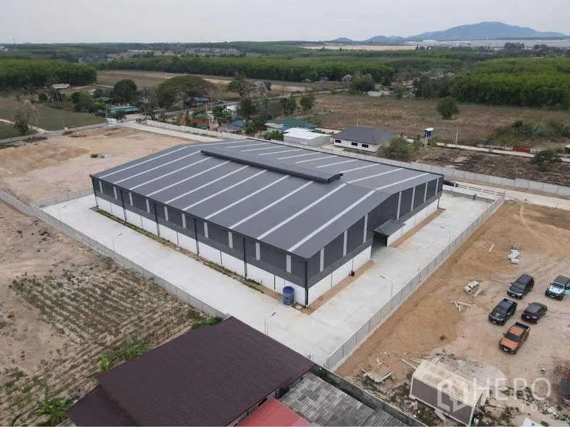 Warehouse for rent or sale in Nikhom Phatthana, Rayong - Rear aerial angle showing the entire warehouse roof, concrete driveways and surrounding green fields in Rayong.