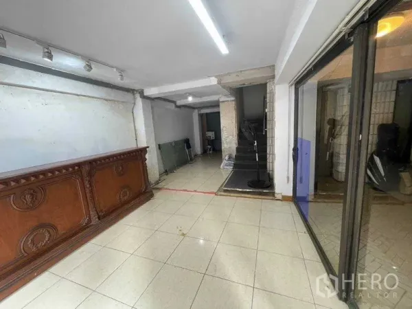 Shophouse for rent in Bang Rak, Bangkok - Open tiled retail hall with a wooden counter, track lighting and an internal staircase.