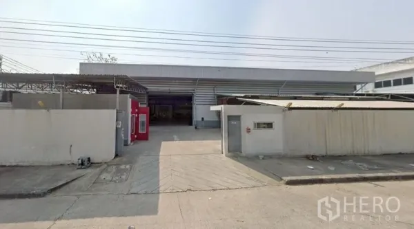 Warehouse for rent in Lam Luk Ka, Pathum Thani - Street-facing gate and wide driveway leading to a metal-clad warehouse facade in Lam Luk Ka.