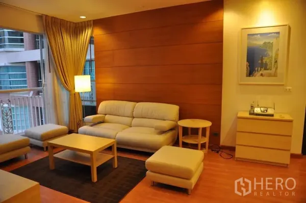Condominium for rent or sale in Khlong Toei, Bangkok - Cozy lounge with cream sofa, ottoman, wood accent wall and large city-facing window.