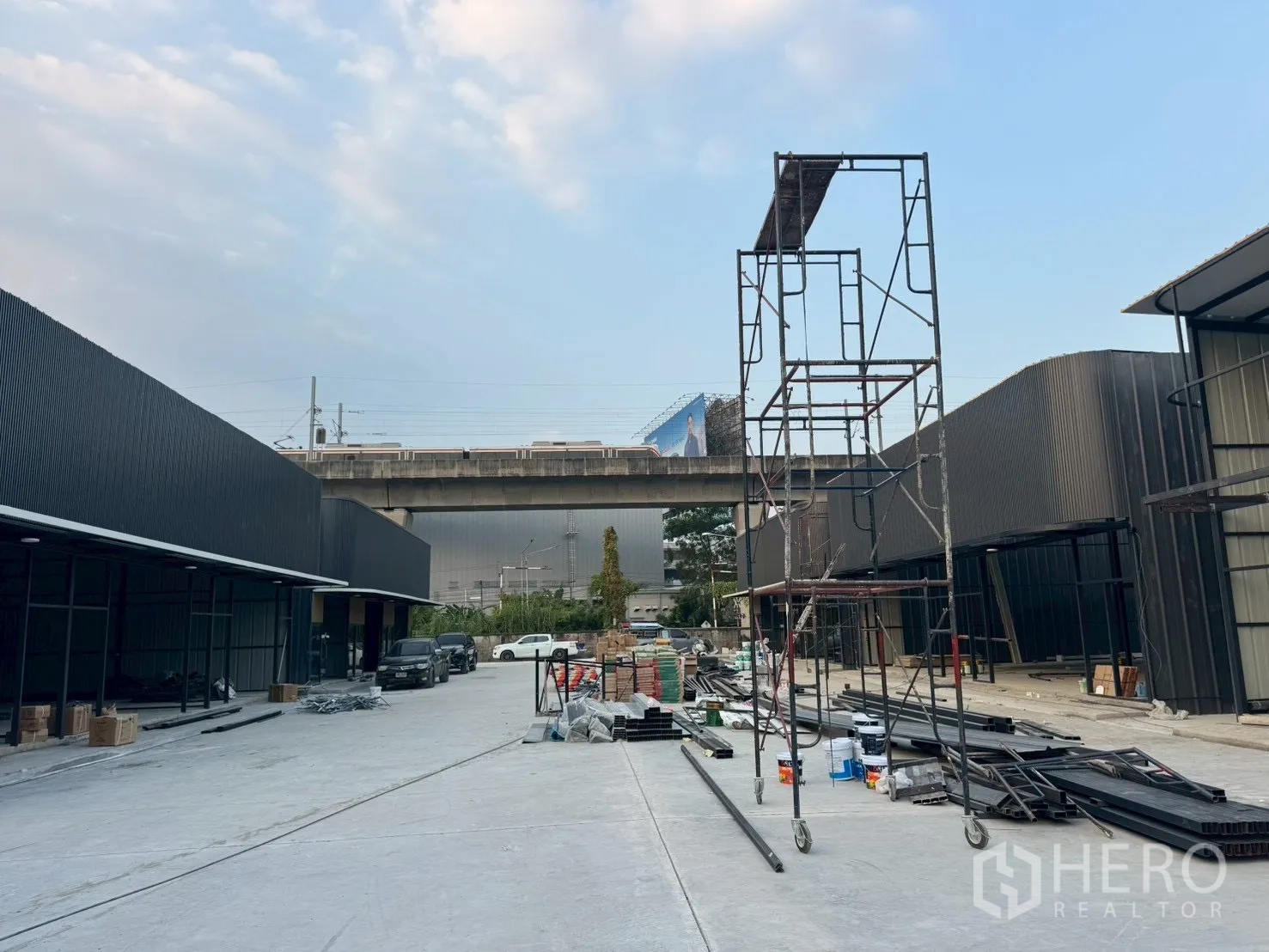Warehouse for rent in Suan Luang, Bangkok - Central lane between two warehouse blocks with scaffolding and building materials, rail viaduct in background.