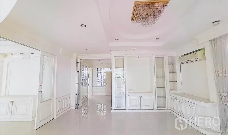 Detached House for sale in Bang Kapi, Bangkok - White living room with glossy tile flooring, recessed lights and built-in display cabinets.
