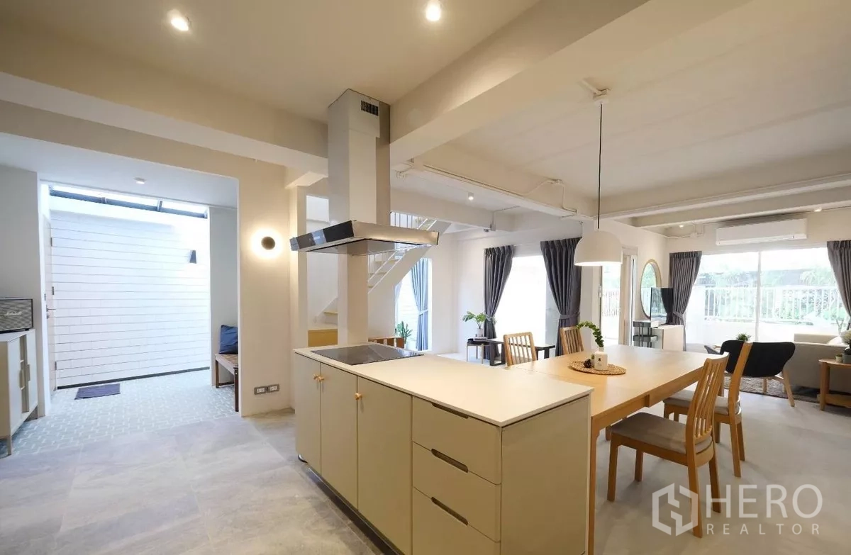 Townhouse for rent or sale in Watthana, Bangkok - Open-plan kitchen and dining area with island, long wooden table and pendant lights.