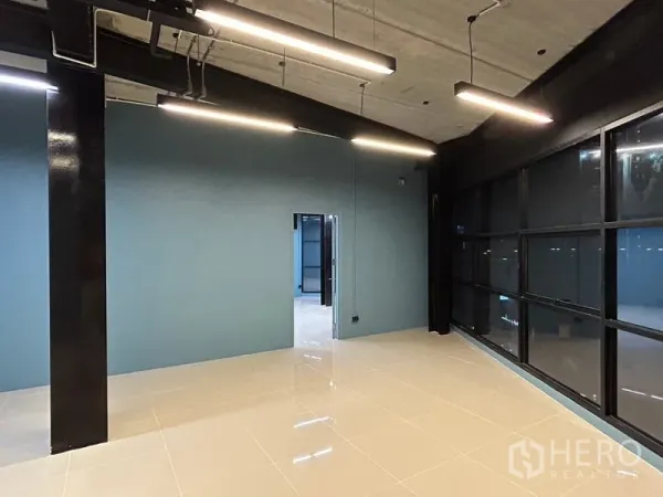 Office Space for rent in Chatuchak, Bangkok - Open-plan office with glossy tile floors, teal feature wall, exposed ceiling and linear LED lights beside black-framed windows.