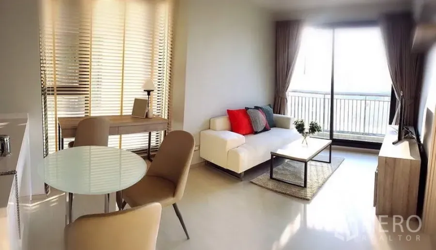Condominium for rent in Khlong Toei, Bangkok - Open-plan living room with white sofa, round dining table, TV console and sliding glass doors to a balcony with city outlook.