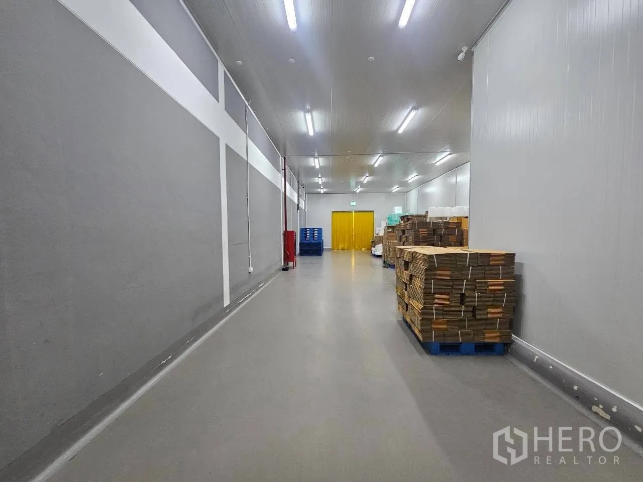 Factory for rent in Mueang Samut Sakhon, Samut Sakhon - Long indoor storage corridor with gray walls, pallets, and bright strip lighting.