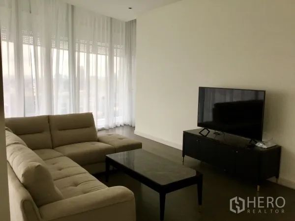Condominium for rent in Pathum Wan, Bangkok - Modern living area with sofa, TV console and marble coffee table framed by sheer curtains and corner windows.