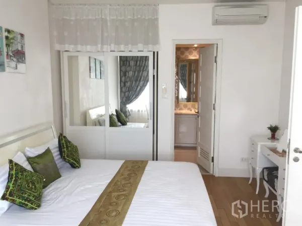 Condominium for rent or sale in Khlong Toei, Bangkok - Calm bedroom with green accent pillows, sliding mirrored wardrobe and door to the ensuite bathroom.