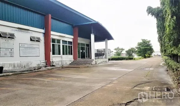 Factory for sale in Lam Luk Ka, Pathum Thani - Side view of factory showing steps to office, long concrete driveway and landscaped verge.