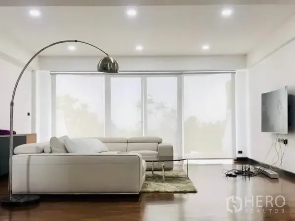 Townhouse for rent or sale in Khlong Toei, Bangkok - Bright living room with white sofas, a curved floor lamp and full-height windows.