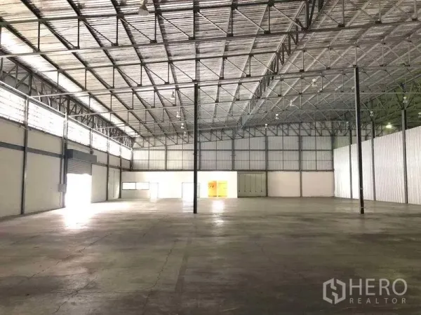 Warehouse for rent in Bang Phli, Samut Prakan - Spacious warehouse interior with high steel truss roof, concrete floor, clerestory windows and roller shutters.