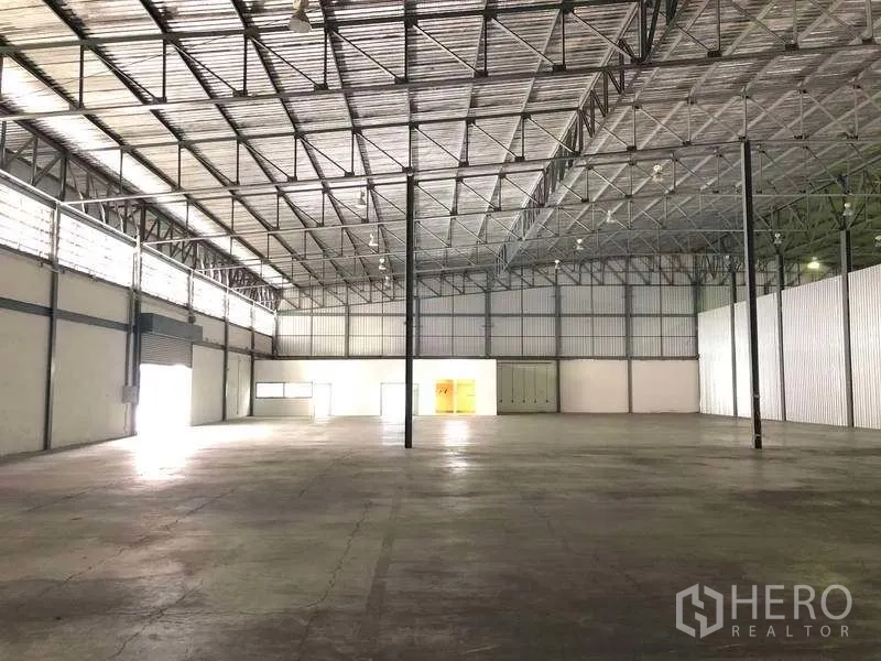 Warehouse for rent in Bang Phli, Samut Prakan - Spacious warehouse interior with high steel truss roof, concrete floor, clerestory windows and roller shutters.