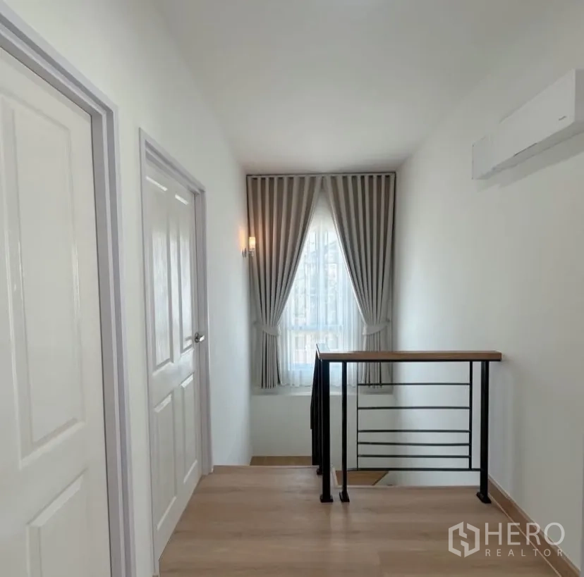 Detached House for rent in Mueang Samut Prakan, Samut Prakan - Stair landing with black metal railing, window drapes and wall sconce.