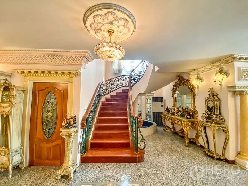 Detached House for rent or sale in Bang Khen, Bangkok - Entry hall featuring a sweeping wooden staircase, decorative ceiling light, and gold console.