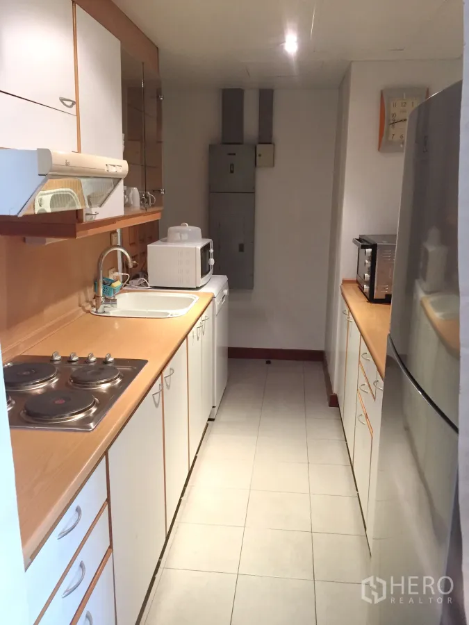 Condominium for rent in Pathum Wan, Bangkok - Galley kitchen with white cabinets, wood countertops, electric cooktop, sink, microwave and full-size refrigerator.