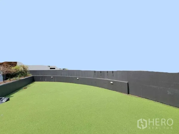 Retail Space for rent in Khlong Toei, Bangkok - Expansive rooftop terrace with artificial grass and high privacy wall under clear sky.