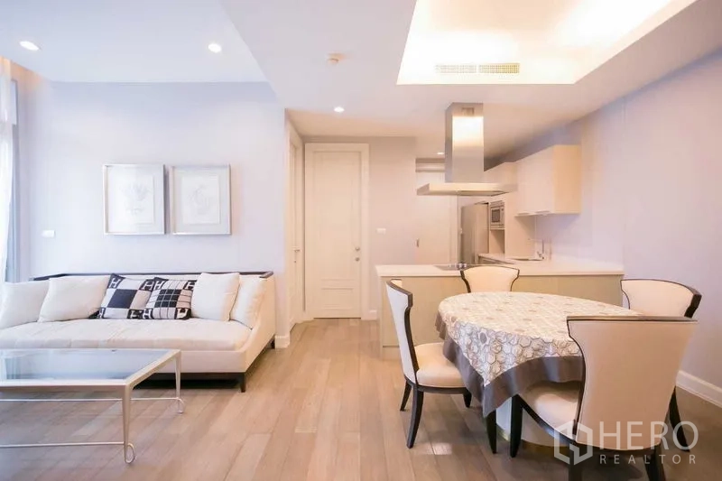 Condominium for rent or sale in Pathum Wan, Bangkok - Living room with cream sofa, glass coffee table and dining area next to an open kitchen.