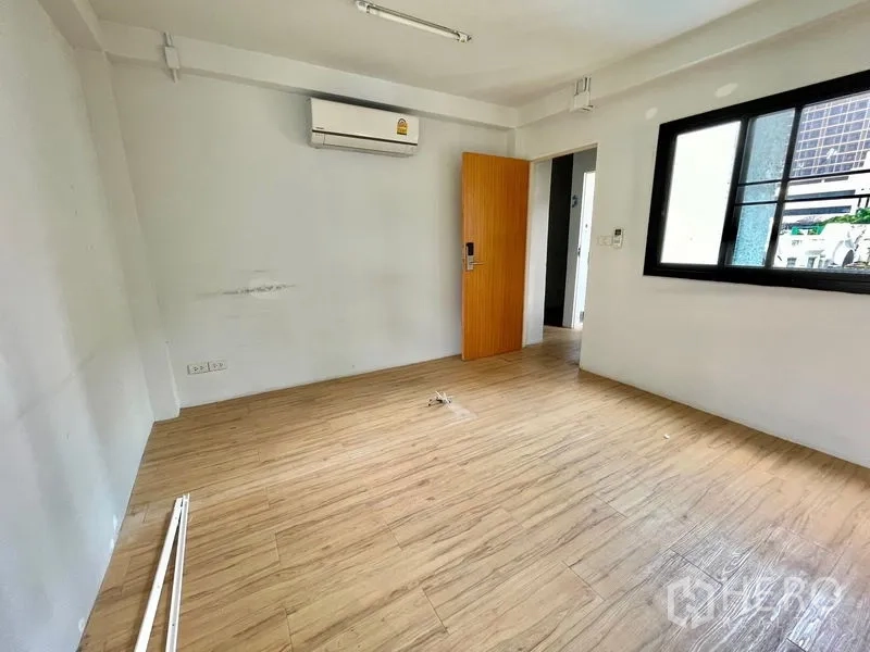 Shophouse for rent in Pathum Wan, Bangkok - Empty air-conditioned room with wood-look flooring and a window, ready for fit-out.