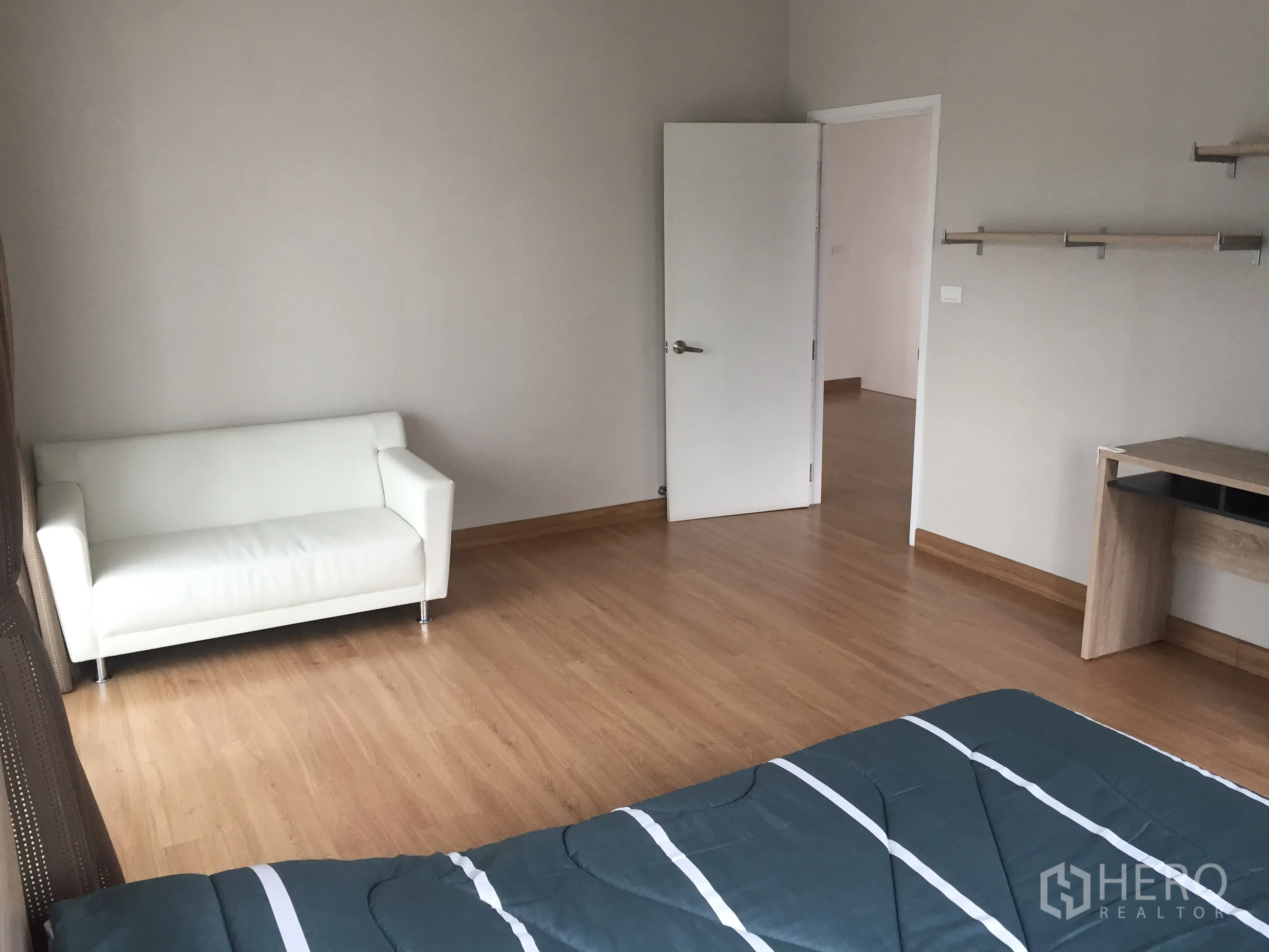 Detached House for rent in Pathum Thani - Bedroom angle showing a white loveseat, work desk, wood floors and doorway.