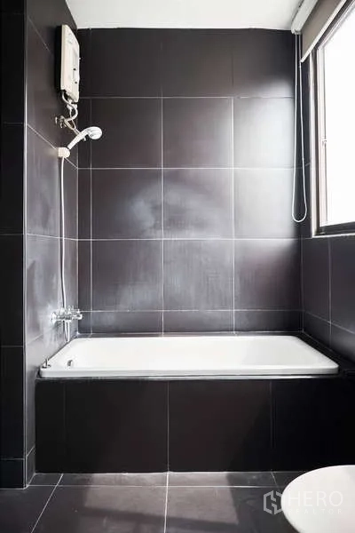 Townhouse for rent in Khlong Toei, Bangkok - Black‑tiled bathroom with bathtub and shower heater beside window