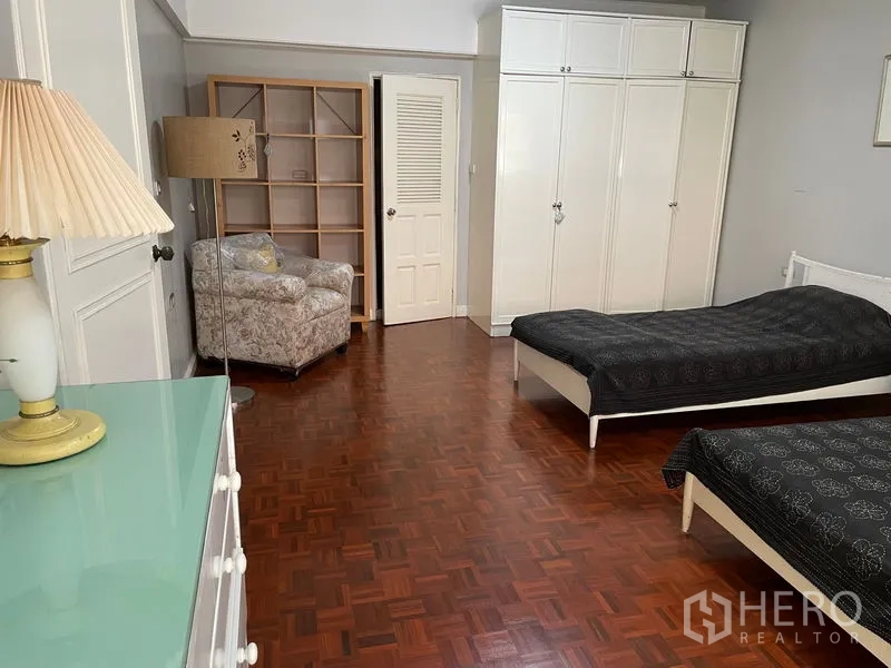 Condominium for rent in Watthana, Bangkok - Spacious bedroom with parquet flooring, twin beds and built-in white wardrobes.