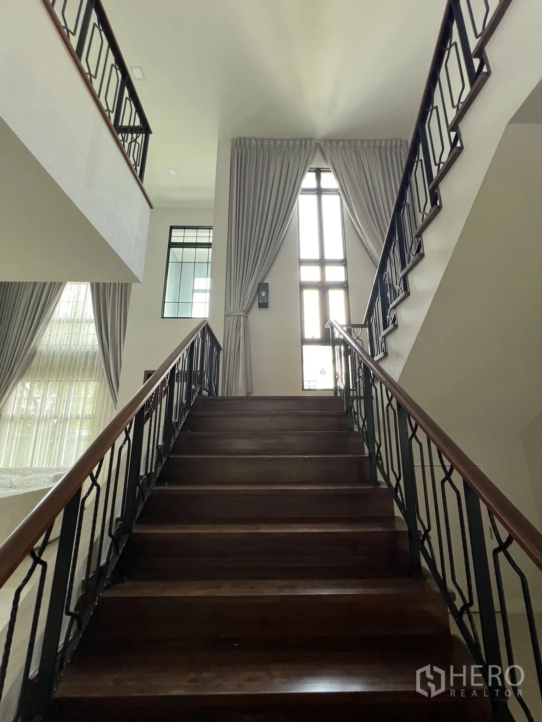 Detached House for rent or sale in Prawet, Bangkok - Wood staircase with wrought-iron balustrade rising toward tall windows.