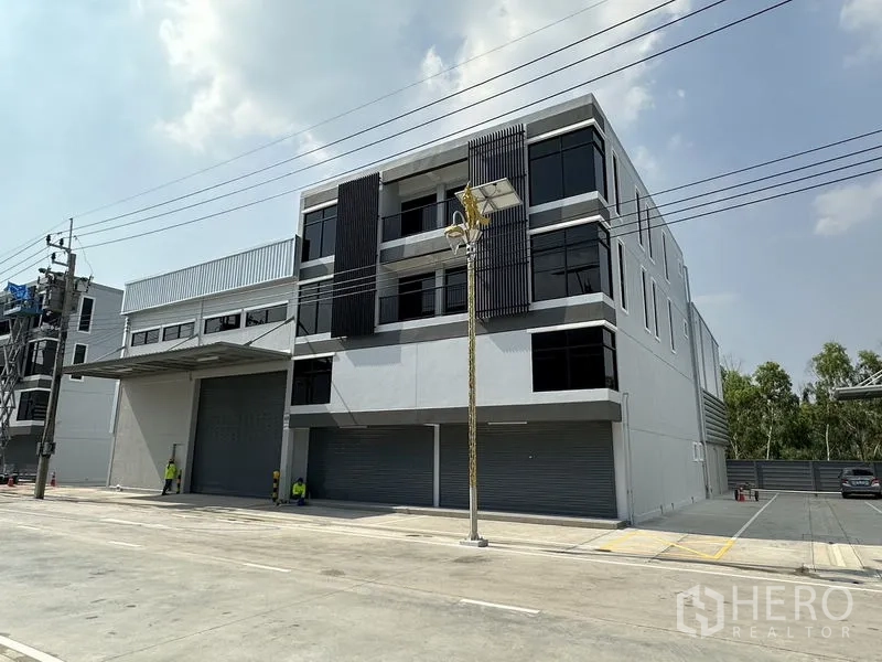 Warehouse for rent in Bang Phli, Samut Prakan - Modern three-storey warehouse exterior with dark window panels and multiple roller shutters.