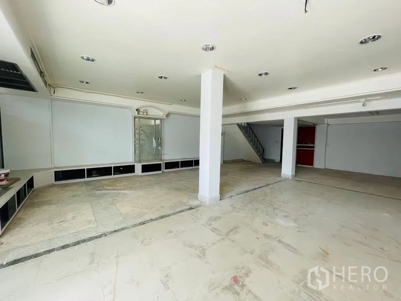Shophouse for rent in Huai Khwang, Bangkok - Spacious open-plan showroom with columns and an internal staircase.