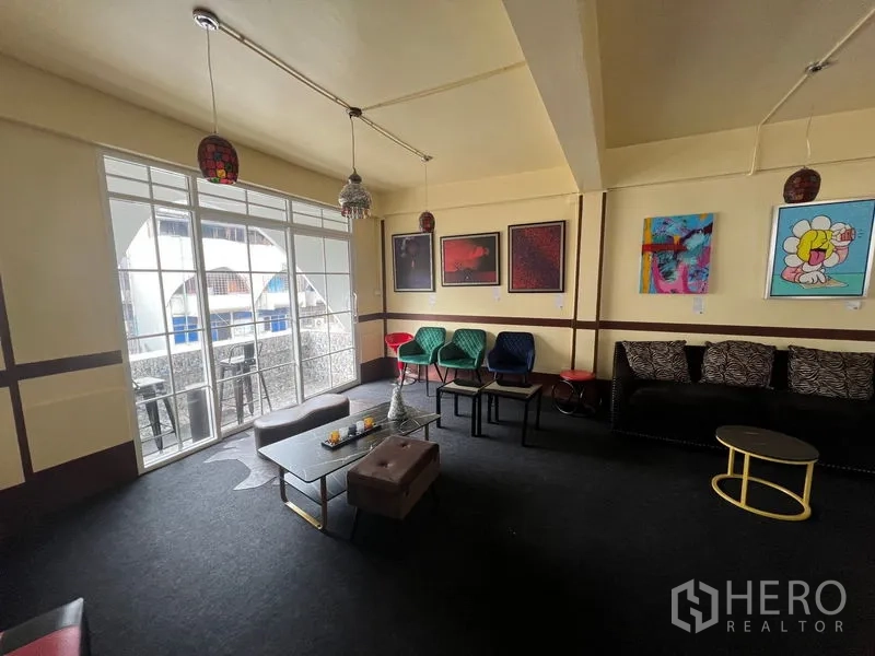 Shophouse for rent in Khlong Toei, Bangkok - Lounge area with sofa seating, colorful chairs and sliding doors opening to a balcony.