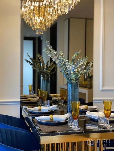 Condominium for rent - Dining table set for four with gold‑rimmed glasses beneath a sparkling crystal chandelier.