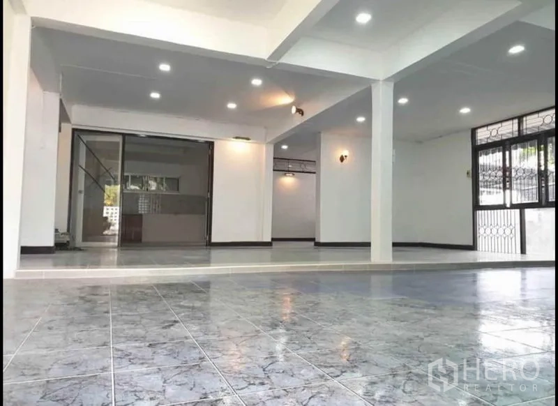 Detached House for rent in Lat Phrao, Bangkok - Bright tiled living area with recessed lighting, pillars and large windows opening toward the kitchen zone.