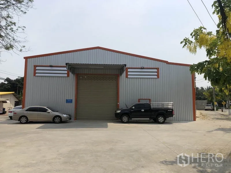 货栈 出租在Bang Yai, Nonthaburi - 仓库正立面，设大型卷帘门、雨棚与宽敞车道停车区。
