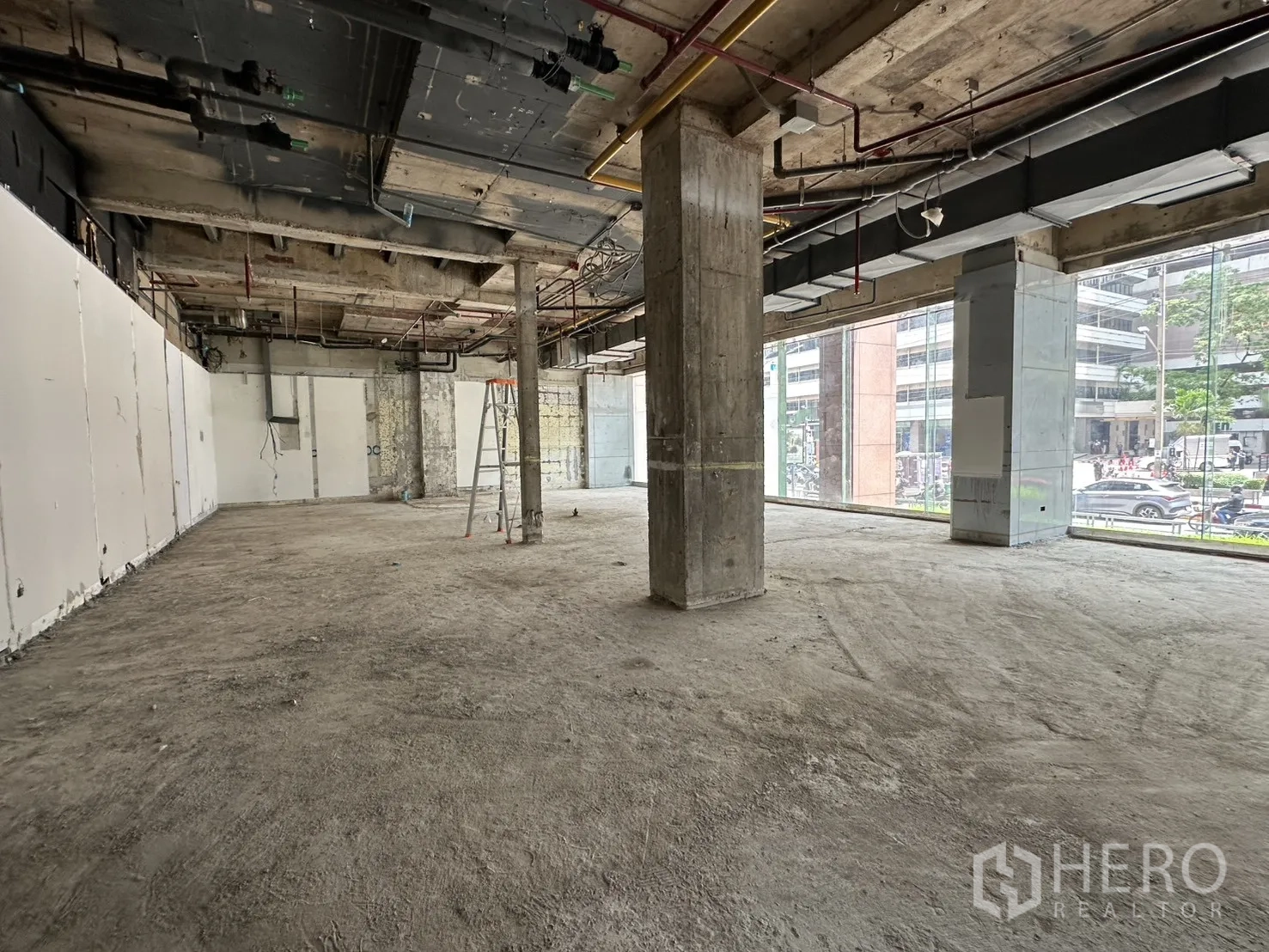 Retail Space for rent in Watthana, Bangkok - Wide retail floor with ladder, high ceilings, and long glass façade overlooking a busy road.