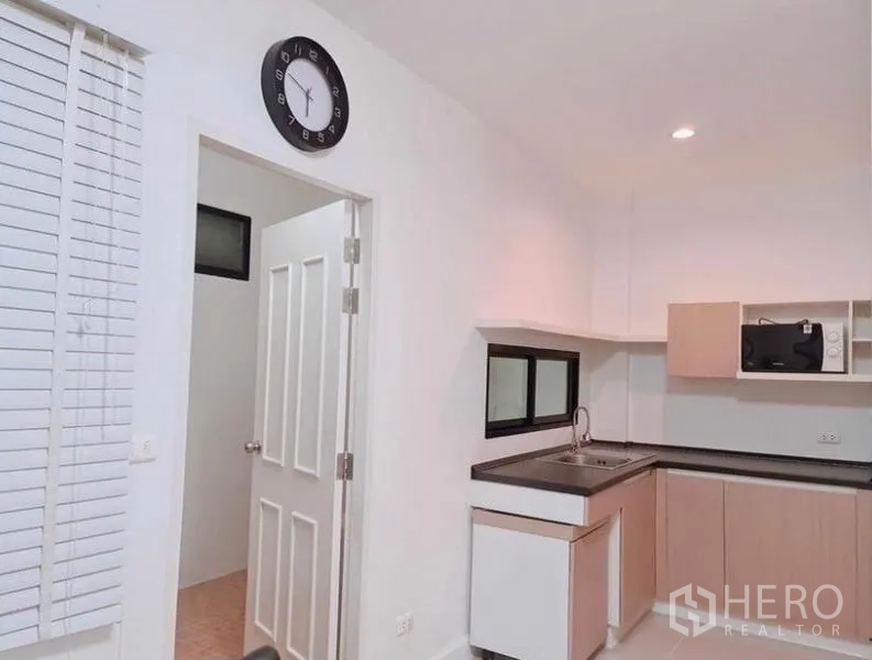 Townhouse for rent in Suan Luang, Bangkok - Compact L-shaped kitchen with upper cabinets, black countertops and utility door