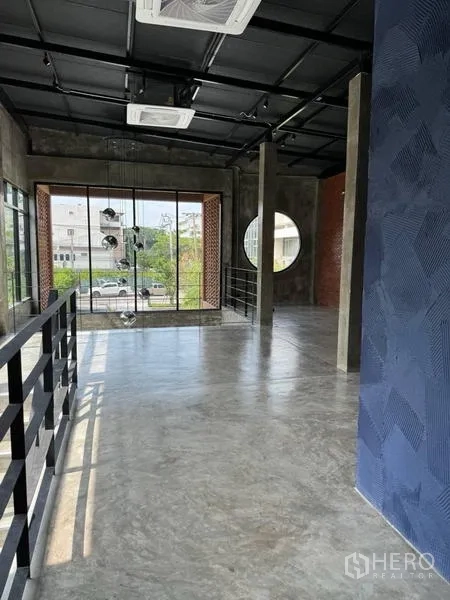 Standalone for rent in Sathon, Bangkok - Loft-style upper floor with polished concrete, exposed black ceiling, circular window and full-height glass overlooking the street.
