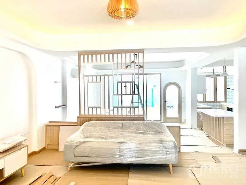 Townhouse for rent in Khlong Toei, Bangkok - Lounge area with wrapped sofa, decorative partition, arched doorway and view toward the kitchen.