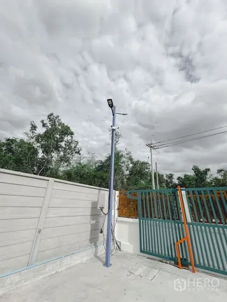 Warehouse for rent or sale in Khlong Luang, Pathum Thani - Close-up of the entrance with a metal sliding gate, pole-mounted lighting and electrical supply.