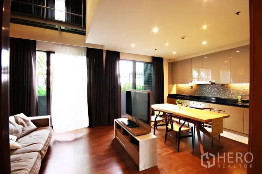 Condominium for rent or sale in Khlong Toei, Bangkok - Open-plan living and kitchen with TV console, dark curtains, and balcony access.