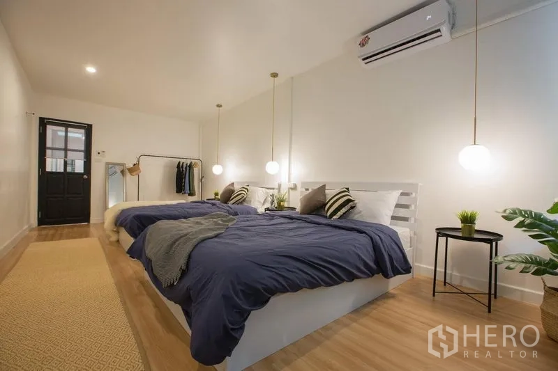 Townhouse for rent in Sathon, Bangkok - Large master bedroom with two double beds, pendant lights, and warm wood floors.