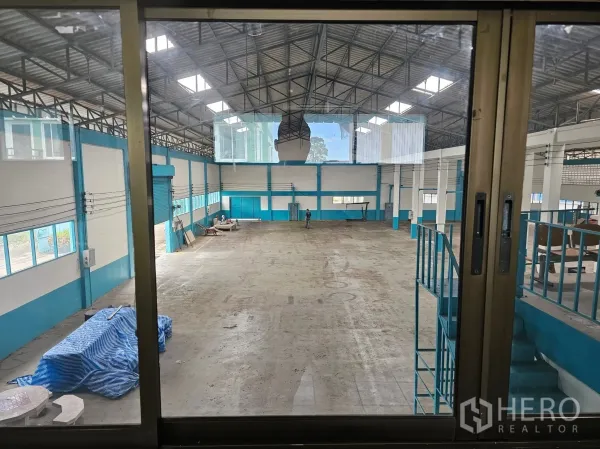 Factory for rent or sale in Mueang Rayong, Rayong - Wide view of the production hall through a glass window showing mezzanine stairs, skylights and clear floor space.